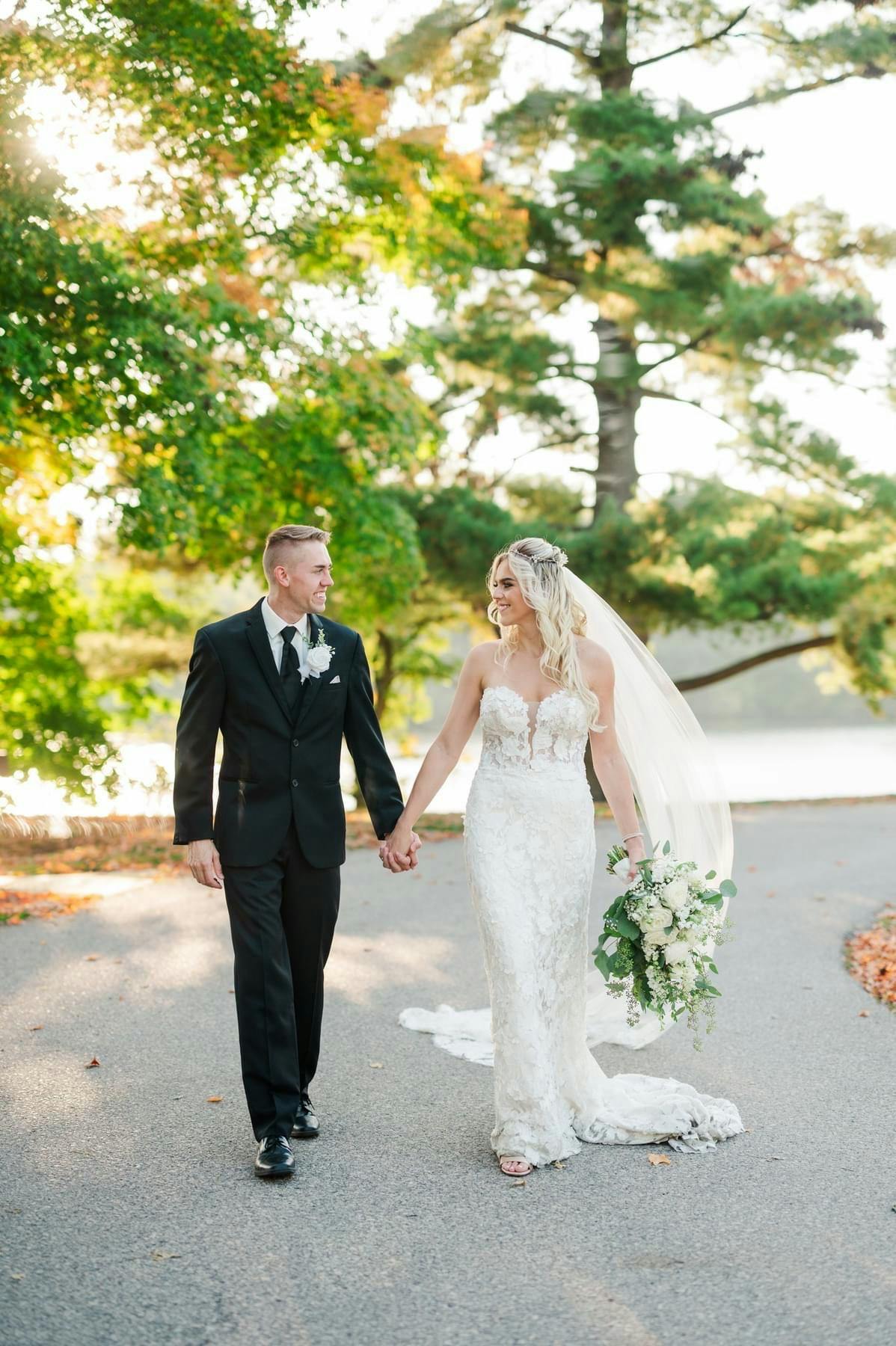 Picture of Bride and groom holding hands walking down a lane with trees in the background