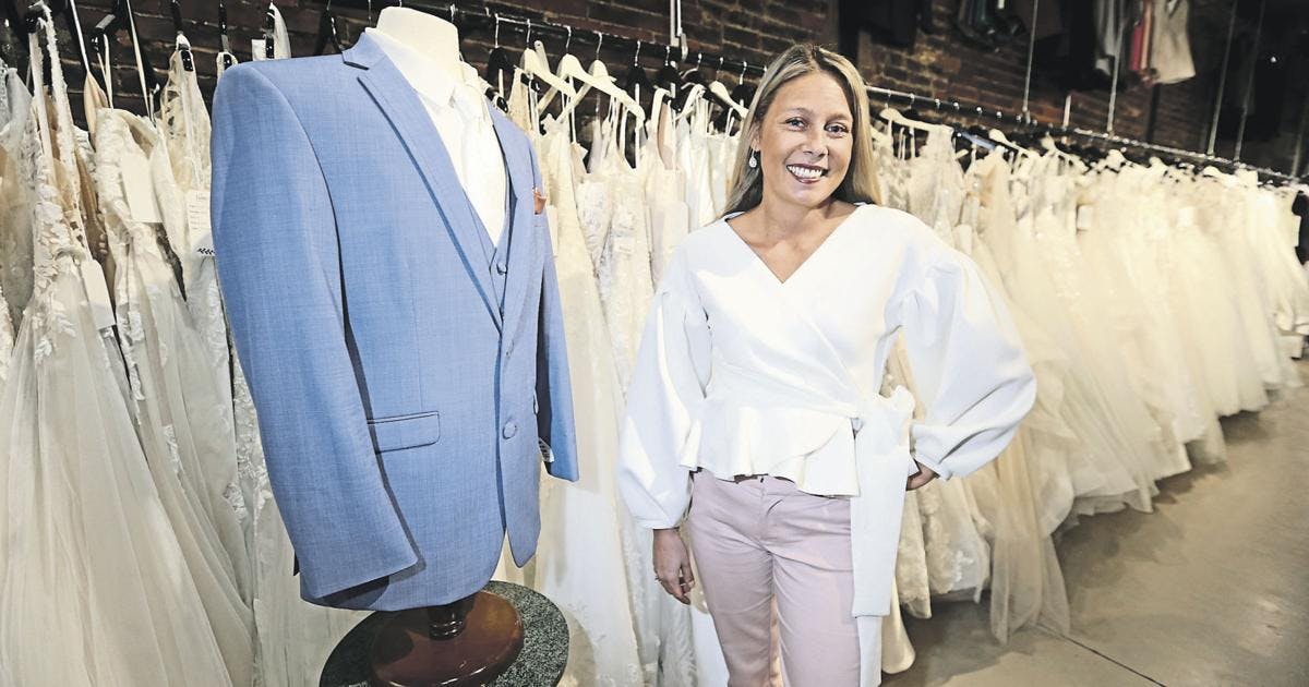 Picture of store owner posing in front of dresses and a blue tux